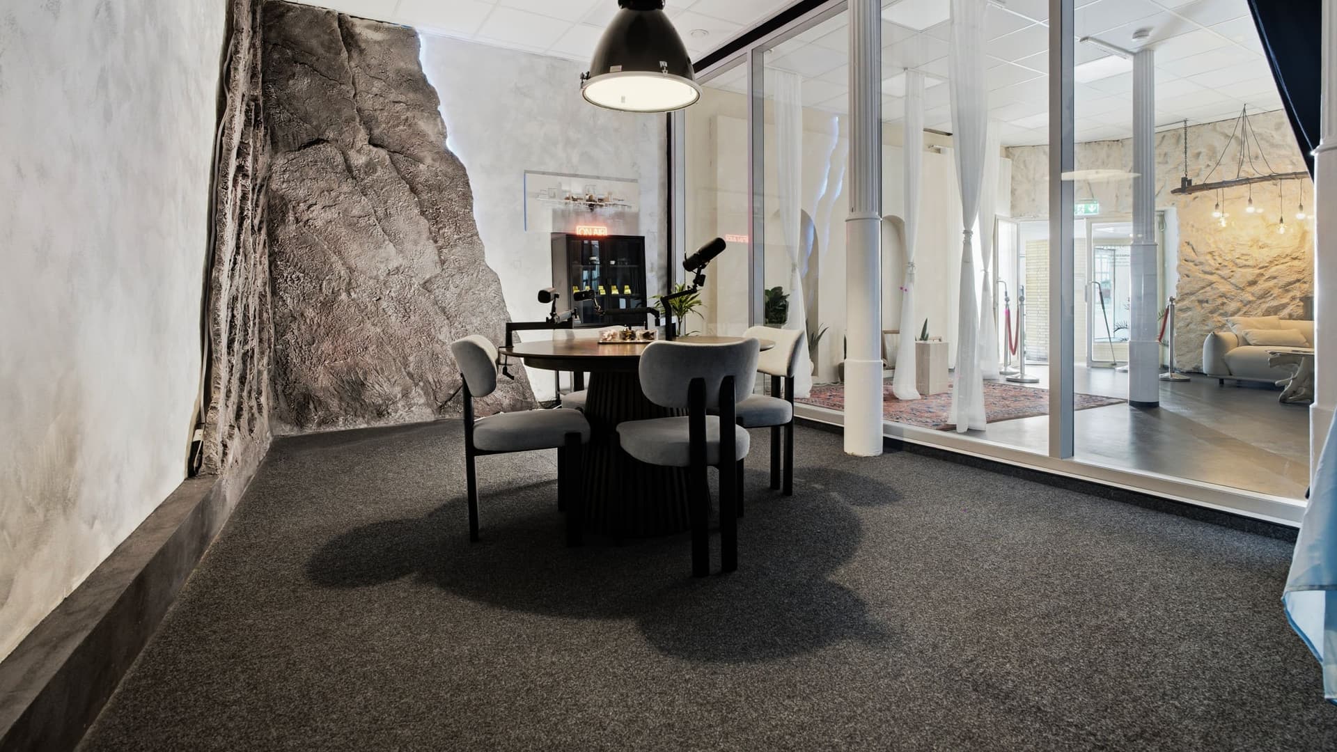 Podcast Room mit rundem Tisch und markanter Steinwand hinter der Glaswand
